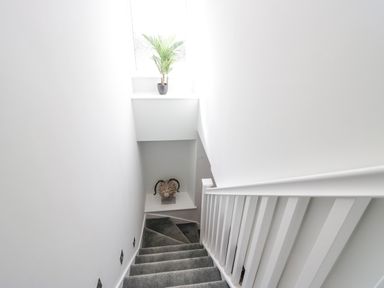 A stairway with gray carpet and white walls with a potted plant on a window ledge and a decorative item on a lower shelf at Crag View Cottage in Stainton with Adgarley near Dalton-In-Furness