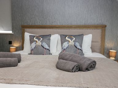 A bedroom with a wooden headboard a bed with bird patterned pillows rolled towels and bedside lamps at Crag View Cottage in Stainton with Adgarley near Dalton-In-Furness
