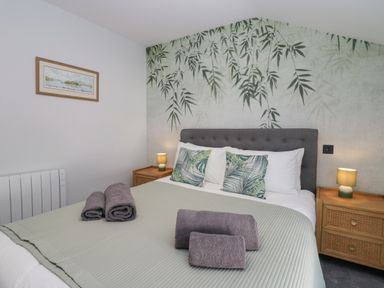 A bedroom with a double bed gray headboard green bedding and patterned pillows two bedside tables with lamps at Crag View Cottage in Stainton with Adgarley near Dalton-In-Furness