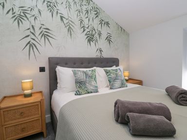 A bedroom with a bed with gray headboard green leaf patterned pillows gray towels on bed and wooden nightstands with lamps at Crag View Cottage in Stainton with Adgarley near Dalton-In-Furness