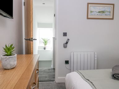 A bedroom with a wooden dresser and a small plant on it a bed with a folded blanket a wall heater and a framed picture at Crag View Cottage Stainton with Adgarley near Dalton-In-Furness