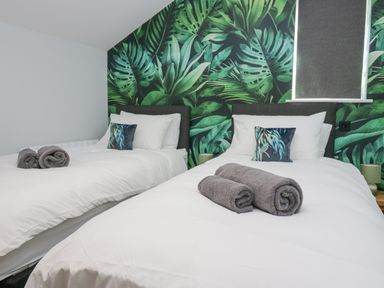 A bedroom with two single beds white bedding rolled towels and leaf patterned wallpaper at Crag View Cottage in Stainton with Adgarley near Dalton-In-Furness