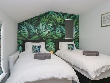 A bedroom with two single beds with white bedding and green leaf patterned wall at Crag View Cottage in Stainton with Adgarley near Dalton-In-Furness