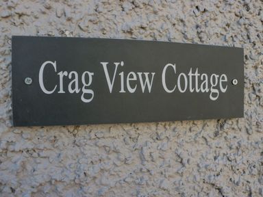 A black sign with white text reading Crag View Cottage mounted on a textured wall at Crag View Cottage in Stainton with Adgarley near Dalton-In-Furness