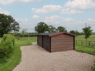 A cabin with a gravel driveway surrounded by grass and trees at Lodge 1 Strensall
