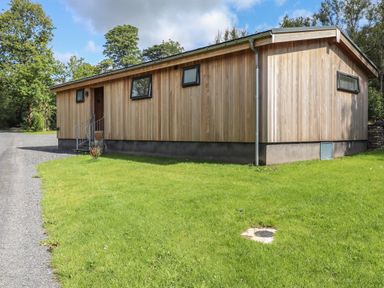 A single-story wooden house with small windows on a grass lawn at Corning Mill View in Haverthwaite