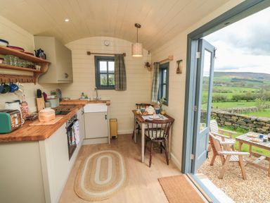 A small kitchen with wooden countertops a sink two chairs and a table next to an open door showing a countryside view at Sheep Cote Shepherds Hut in Chop Gate near Stokesley