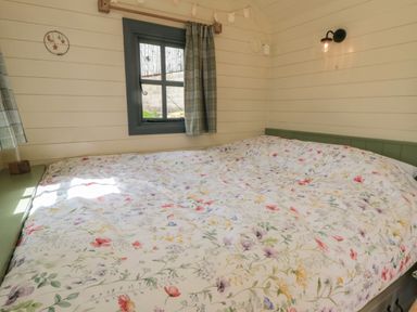 A bedroom with a floral bedspread a window with curtains and a wall light at Sheep Cote Shepherds Hut in Chop Gate near Stokesley