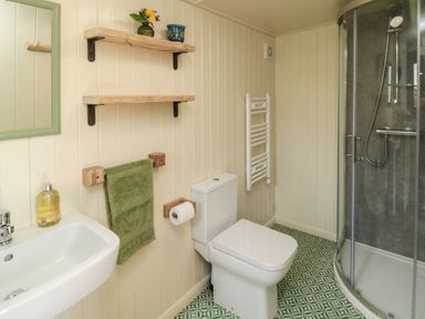A bathroom with a toilet, shower, sink, green towel, two wooden shelves with pots, and patterned floor at Sheep Cote Shepherds Hut Chop Gate near Stokesley