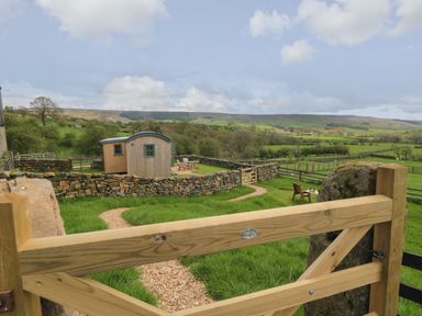 A wooden gate opening to a stone path and a small wooden hut in a fenced grass field at Sheep Cote Shepherds Hut in Chop Gate near Stokesley