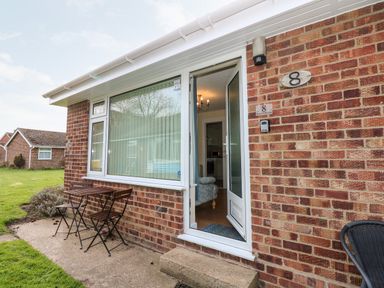 The entrance of a brick house with an open white door a small wooden table and two chairs outside at 8 Royal Chalet Park in Mundesley