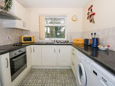 A kitchen with white cabinets black countertops a window with vertical blinds and patterned floor tiles at 8 Royal Chalet Park in Mundesley