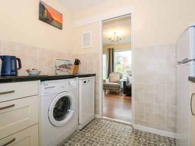 A kitchen with a washing machine dishwasher kettle and knives with a view into a living room at 8 Royal Chalet Park in Mundesley