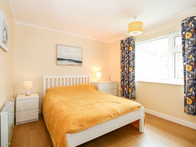 A bedroom with a bed covered in an orange blanket bedside tables with lamps and windows with patterned curtains at 8 Royal Chalet Park in Mundesley
