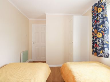 A bedroom with two single beds covered in yellow blankets white wardrobe white door and floral curtains at 8 Royal Chalet Park in Mundesley