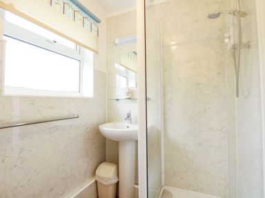 A bathroom with a window pedestal sink small trash bin shower area and a towel bar at 8 Royal Chalet Park in Mundesley