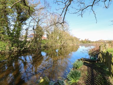 A river with trees and shrubs alongside houses in the background at 8 Royal Chalet Park in Mundesley