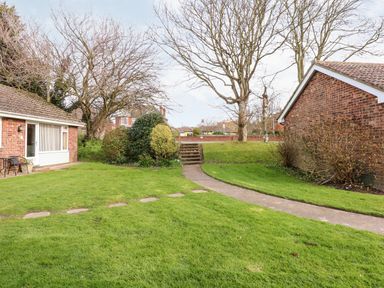 A garden area with a footpath leading to steps between two brick buildings at 8 Royal Chalet Park in Mundesley
