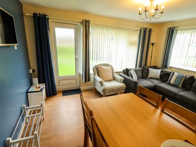 A living room with a dining table chairs a sofa an armchair and a door at 8 Royal Chalet Park in Mundesley