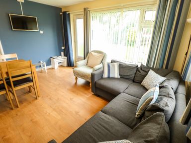 A living room with a gray sofa and armchair near a large window with vertical blinds at 8 Royal Chalet Park in Mundesley