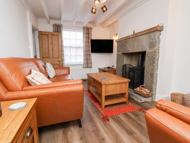 A living room with orange leather sofas a wooden coffee table and a stone fireplace at Braeside in Fylingthorpe