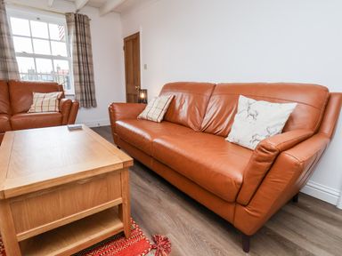 A sitting room with two brown leather sofas a wooden coffee table and a window with plaid curtains at Braeside in Fylingthorpe