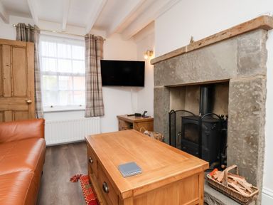 A living room with a leather sofa a wooden coffee table a stone fireplace and a wall mounted television at Braeside in Fylingthorpe