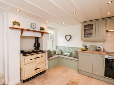 A kitchen with a beige stove an L-shaped bench by a window and green cabinets at Braeside in Fylingthorpe