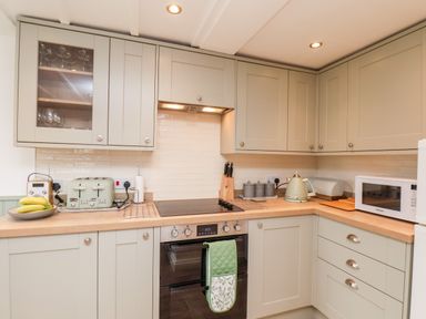 A kitchen with light green cabinets a wooden countertop a stove toaster kettle microwave and a bowl with bananas at Braeside in Fylingthorpe