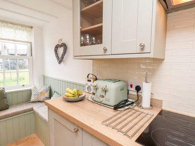 A kitchen corner with a countertop holding a toaster paper towel and fruit bowl next to a window seat with cushions at Braeside Fylingthorpe