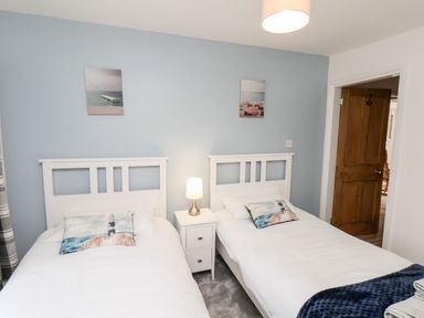 A bedroom with two single beds a nightstand with a lamp and two pictures on a blue wall at Braeside in Fylingthorpe
