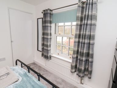 A bedroom window with plaid curtains and a blue roller blind a bed with folded towels and a door in a room at Braeside in Fylingthorpe