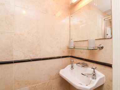 A bathroom with a white sink with two taps a glass shelf holding two patterned containers and a large mirror above Braeside in Fylingthorpe