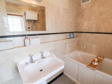 A bathroom with a sink and a bathtub with a rubber duck on a bath tray at Braeside in Fylingthorpe