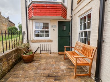 A small outdoor patio with a wooden bench a potted plant and a green door at Braeside in Fylingthorpe