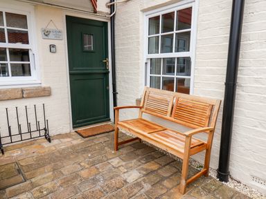 A wooden bench outside a green door and white brick building at Braeside in Fylingthorpe