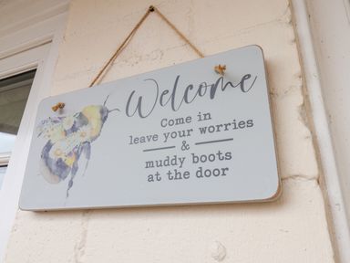 A welcome sign with a bee illustration hanging on a wall near a door at Braeside in Fylingthorpe