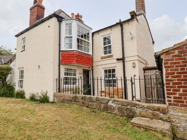 A brick house with white painted walls and a bay window with red tiles a black metal fence and a grassy yard at Braeside in Fylingthorpe