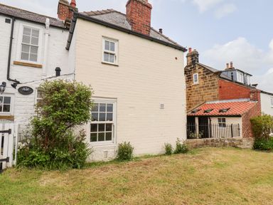 Exterior view of a cottage with white painted brick walls and chimney with garden and grass in front at Braeside in Fylingthorpe