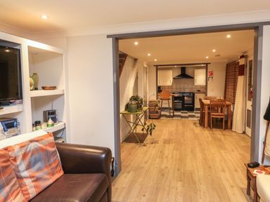 A living room with a leather sofa and an open view into a kitchen with a dining table at Lime Court Barn in Sheepwash