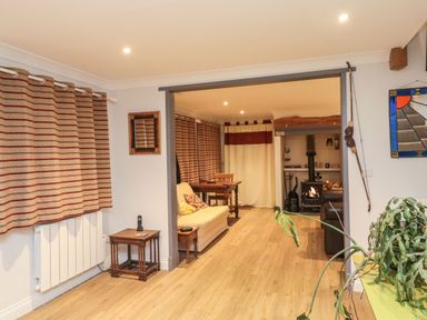 A living room with wooden floors a small table with a phone striped curtains a sofa and a wood stove at Lime Court Barn in Sheepwash