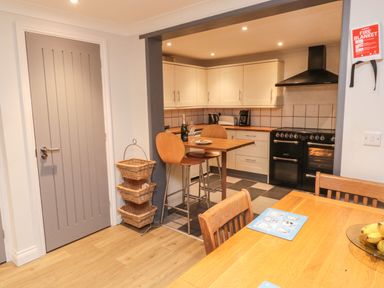 A kitchen with white cabinets black stove and wooden chairs at Lime Court Barn in Sheepwash
