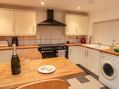 A kitchen with wooden countertops a black stove and oven a white washing machine and a wooden table with a bottle of champagne glasses and a plate of cookies at Lime Court Barn in Sheepwash