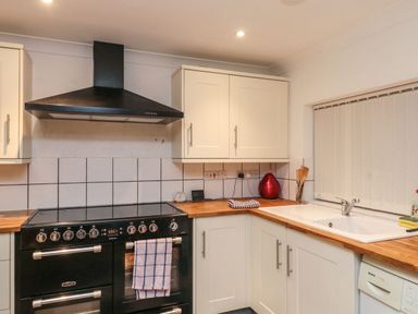 A kitchen with a black stove and oven and white cabinets and a sink with a window blind at Lime Court Barn in Sheepwash