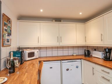 A kitchen with white cabinets wooden countertops a microwave kettle toaster coffee maker and two under counter appliances at Lime Court Barn in Sheepwash