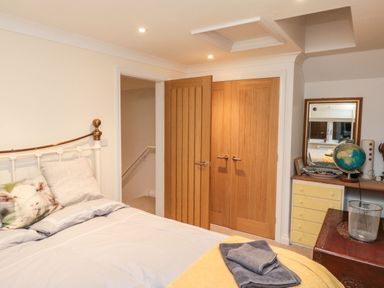 A bedroom with a bed pillows wooden doors dresser with a globe and a mirror at Lime Court Barn in Sheepwash