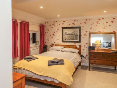 A bedroom with a bed with yellow blanket and folded towels a wooden dresser with a lamp and mirror and red curtains at Lime Court Barn in Sheepwash