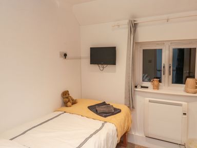A bedroom with a bed a teddy bear a wall-mounted TV and a window with pottery on the sill at Lime Court Barn in Sheepwash