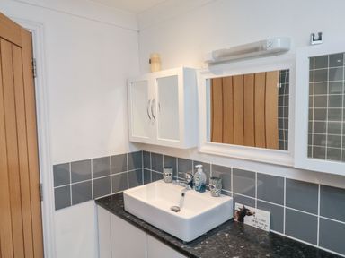 A bathroom sink with mirror cabinets and soap dispenser at Lime Court Barn in Sheepwash