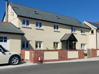 A two-story house with multiple windows and a tiled roof and a white car parked in front at Lime Court Barn in Sheepwash